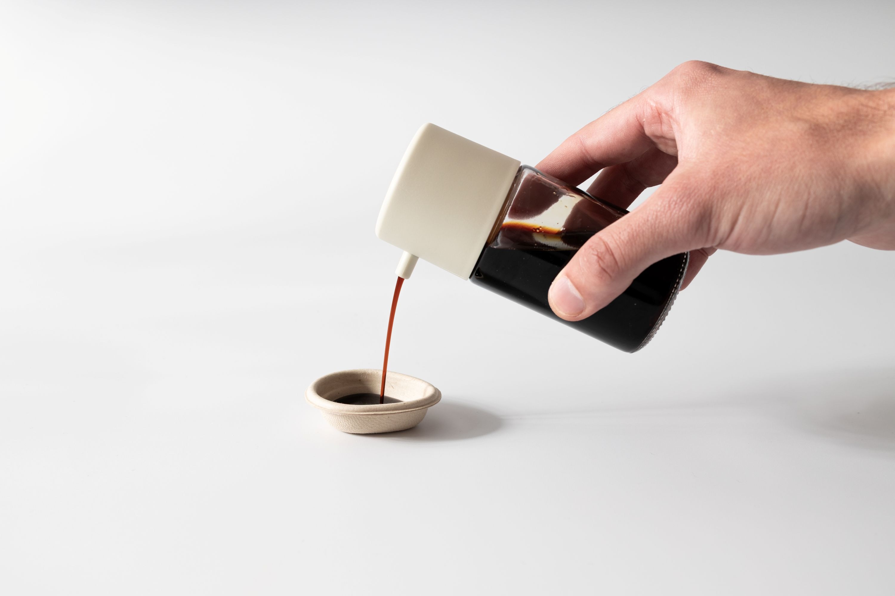 A hand pouring soy sauce from a bottle into a small dish.
