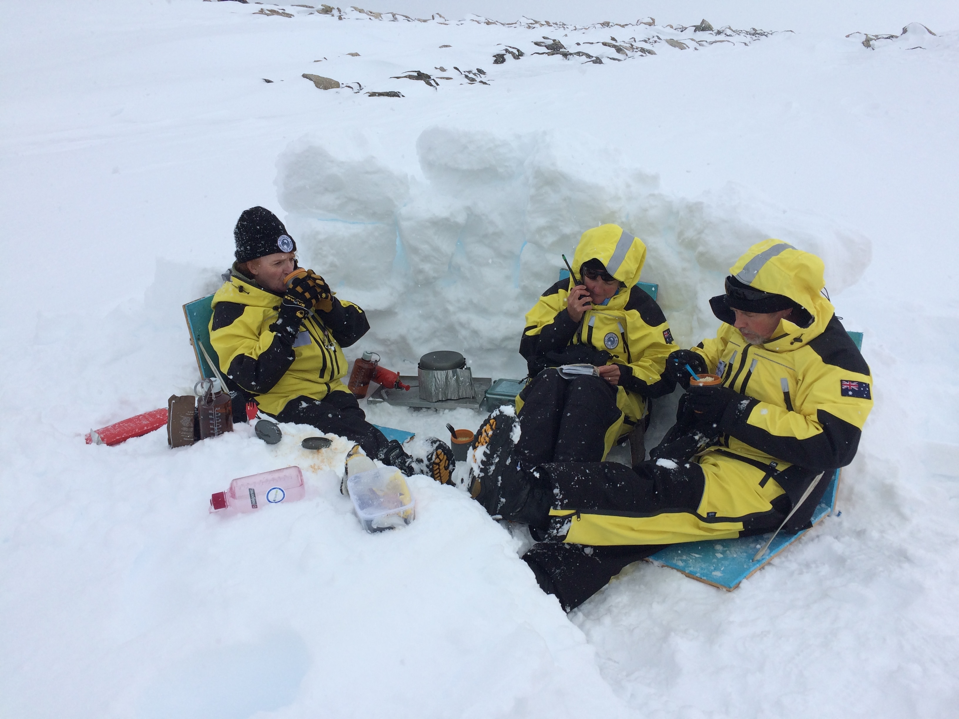 Three people in yellow and black snow gear in an icy dugout.