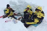 Three people in yellow and black snow gear in an icy dugout.