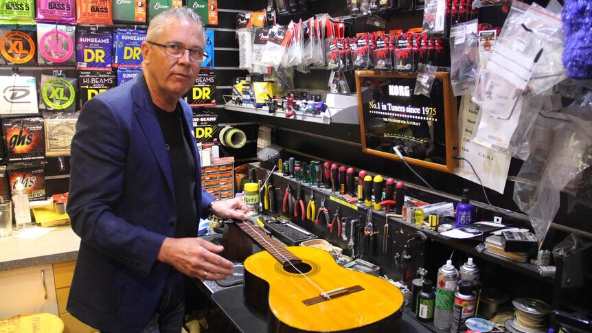 Mr Hoskins strings a guitar in front of a range of merchandise.
