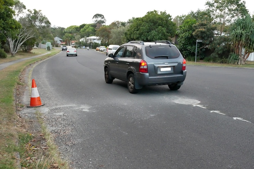 A car drives over a pothole filled with concrete in a suburban street.