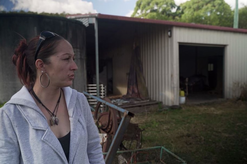 A side profile of a woman, serious expression, standing in front of a shed