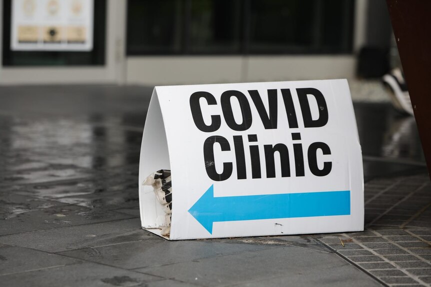 A close-up photo of a sign saying 'COVID clinic' on a tiled floor.