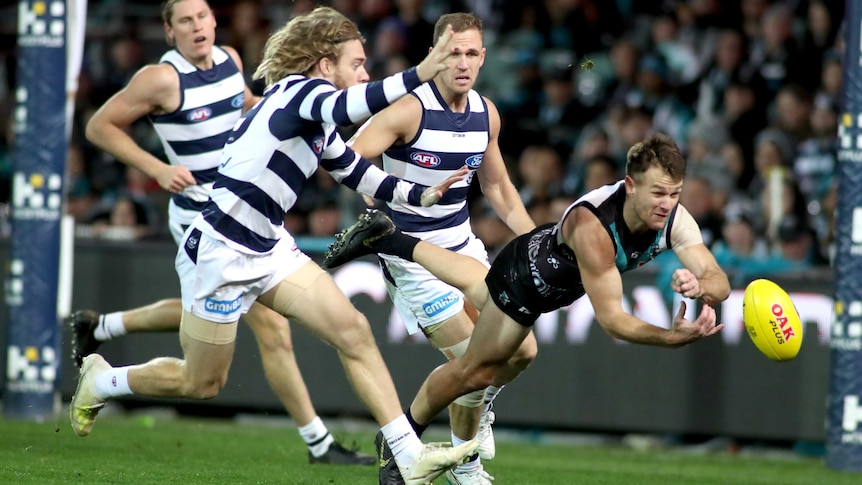 An AFL player handballs at full stretch as a handful of opposition players try to get to him.