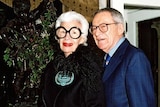 An elderly woman in large, dark framed glasses and a man in a suit