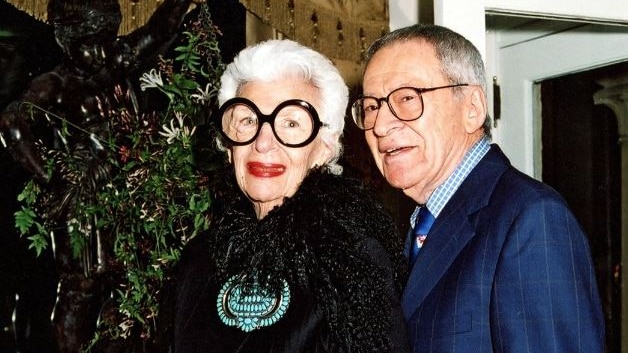 An elderly woman in large, dark framed glasses and a man in a suit