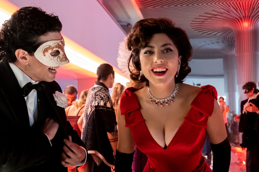 Italian woman with elegantly styled dark hair wears red satin gown, black gloves and diamond necklace at masquerade party