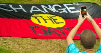A man takes a photo of an Indigenous flag with "change the date" written on it.