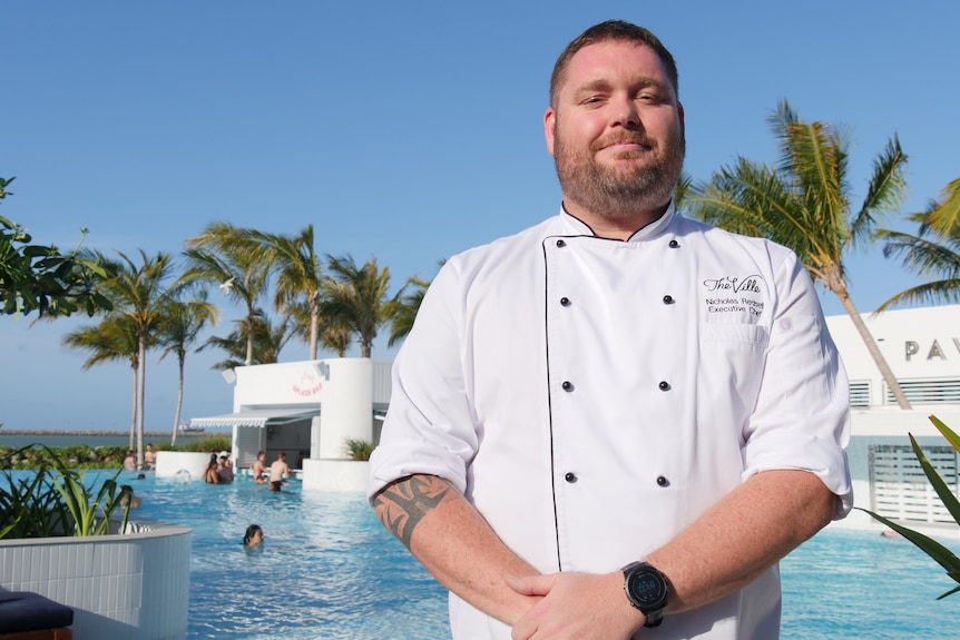 A chef, wearing his white uniform, stands in front of a swimming pool at a hotel