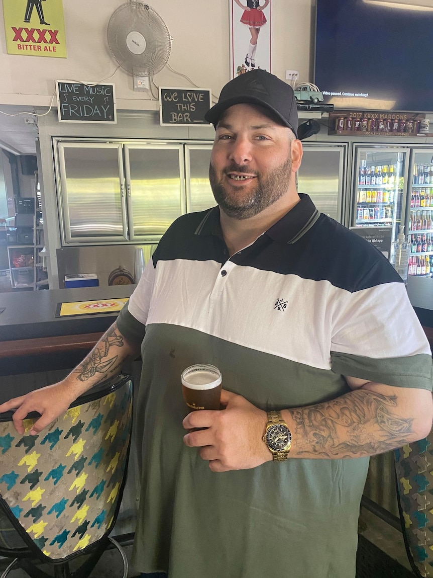 A man stands in front of a bar holding a beer 
