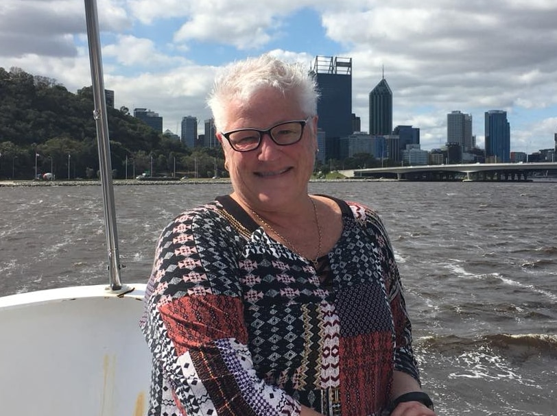 A woman sitting on a boat in a river with a city skyline in the background on a cloudy day