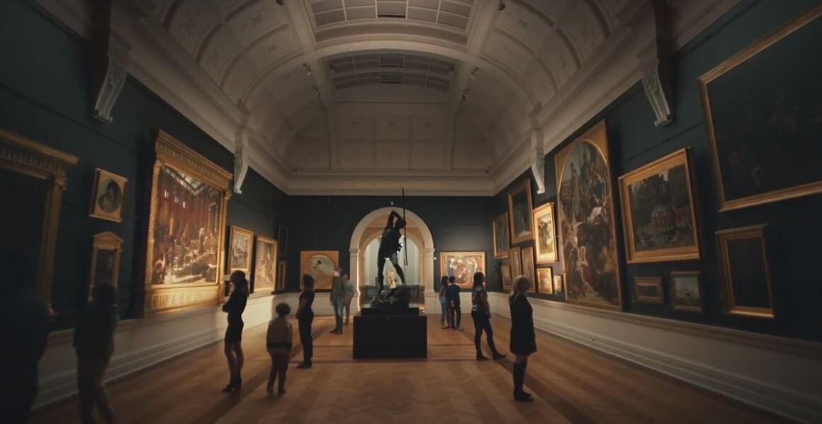 people walking inside an art gallery looking at paintings hanging on a wall