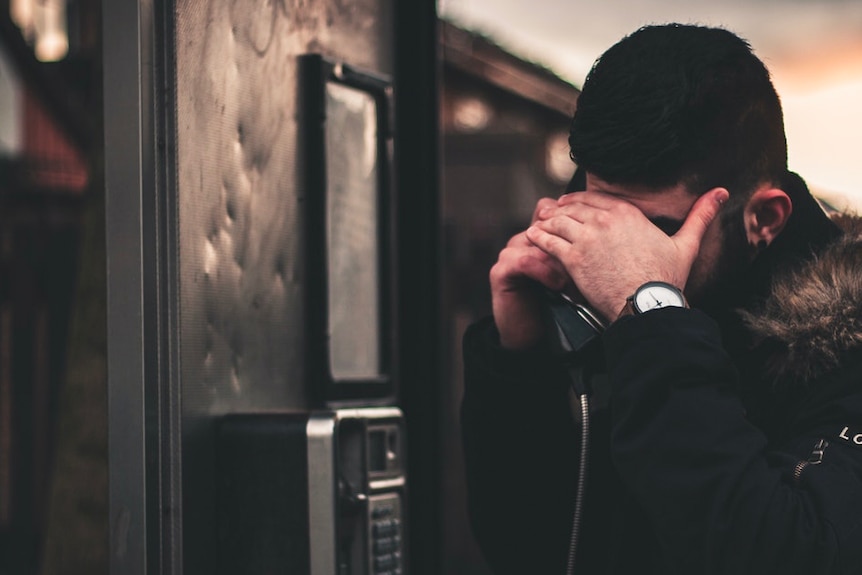 A man covers his face whilst using a payphone