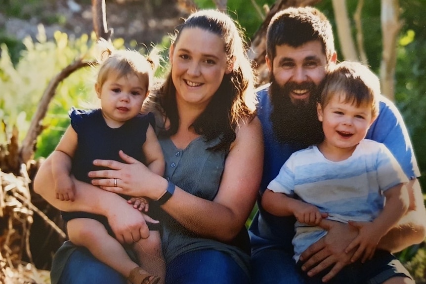 A man with a long beard, a woman and two young children pose for a family photo together.