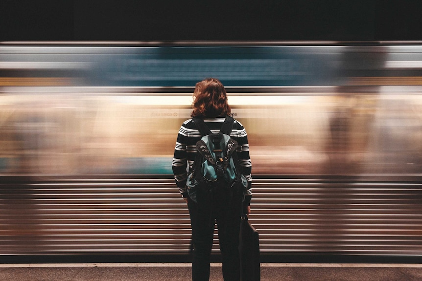 A woman watches as a train goes past her while she stands on the platform