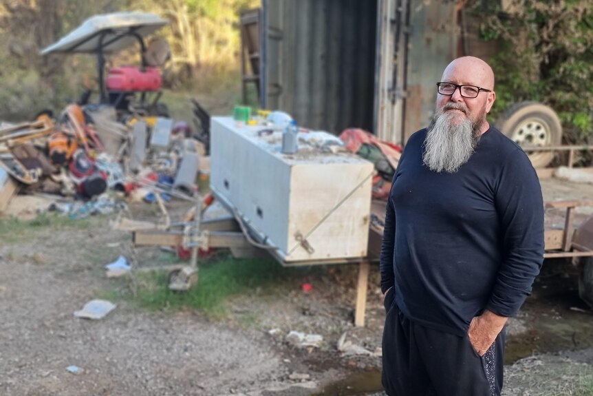 man with beard looks at camera with rubbish in the background