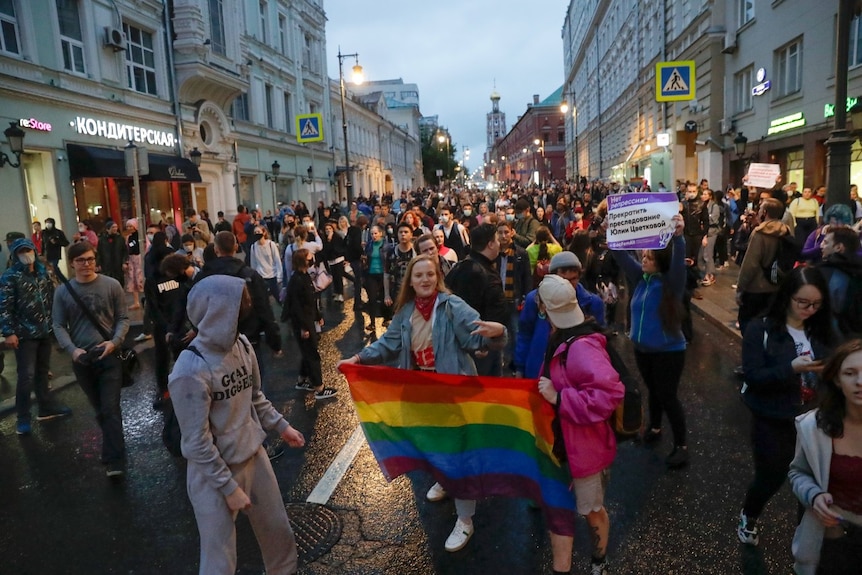 A large group of people on a street, including some holding rainbow flags