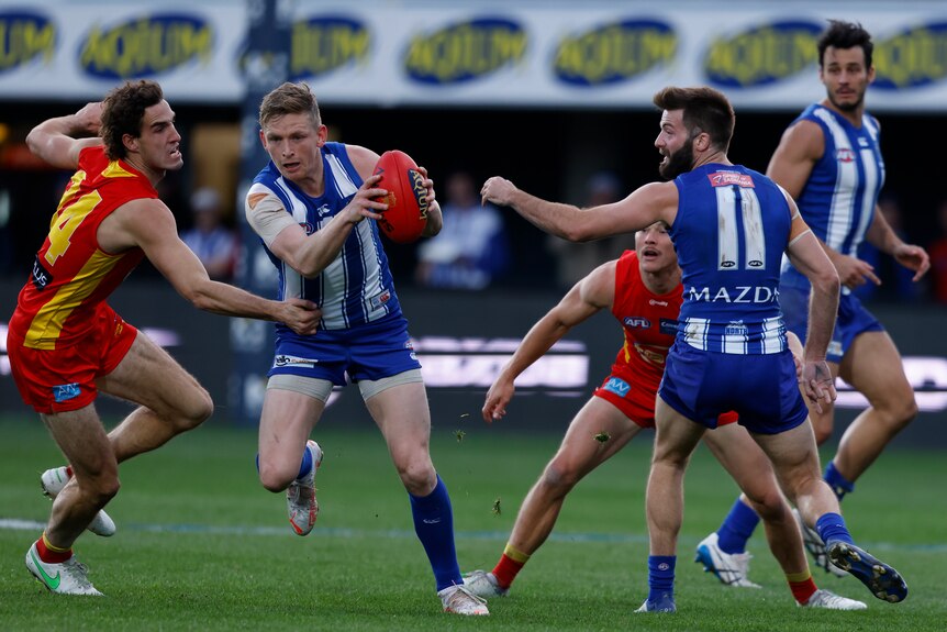 AFL player running with the ball with opposition players surrounding him during a match