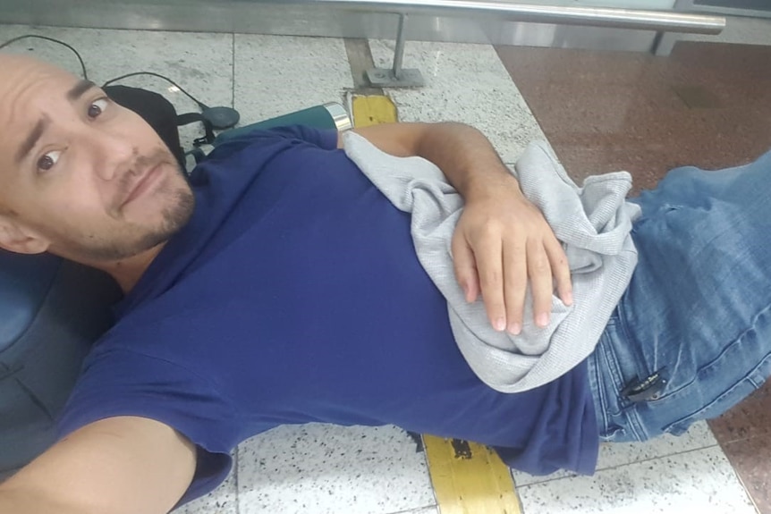 man lies on tiled ground resting head on bag