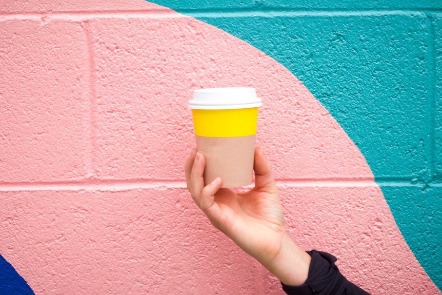 Woman holding coffee cup in front of wall