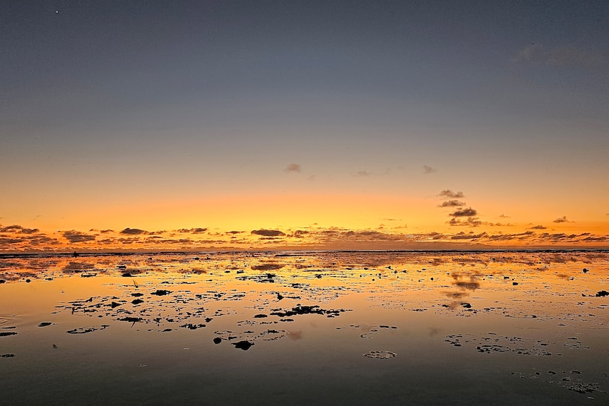 Reflection of yellow and orange sunrise in water at the bottom of shot