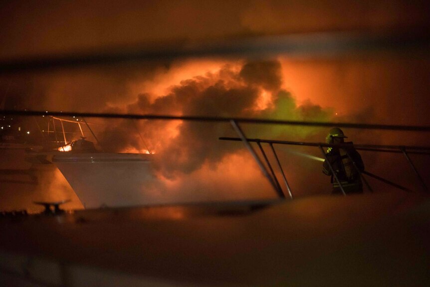 A firefighter shines a torch into smoke billowing from a boat fire in Hobart.