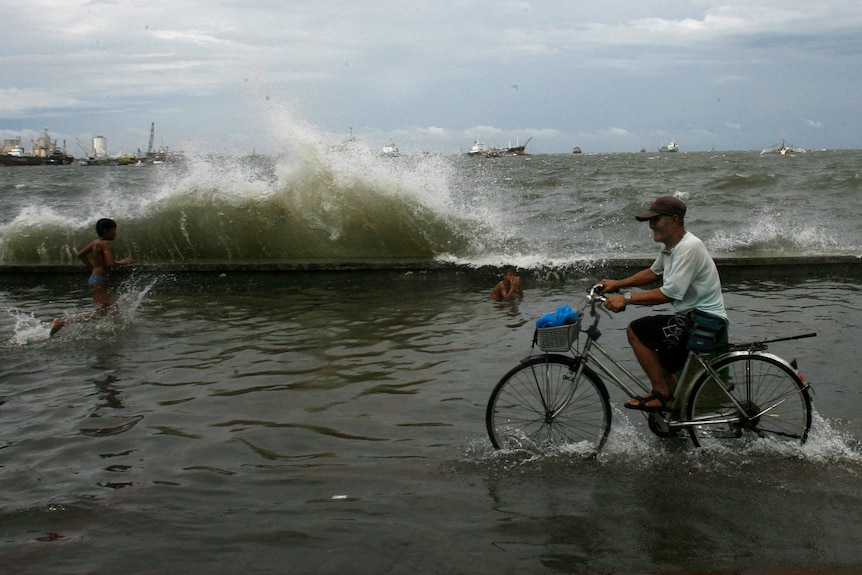 Picture of a man riding a bicycle through flood water 
