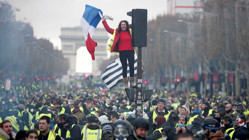 A protester wearing yellow vest stands on the red light on the Champs-Elysee with the Arc de Triopmhe in background.