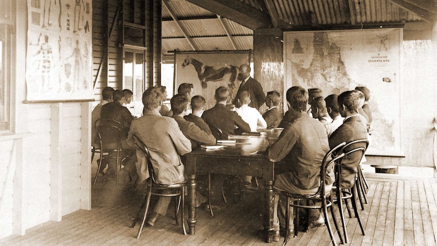 A historic photo of men sitting on an enclosed verandah looking at a map of Queensland and a horse at the UQ Gatton campus.