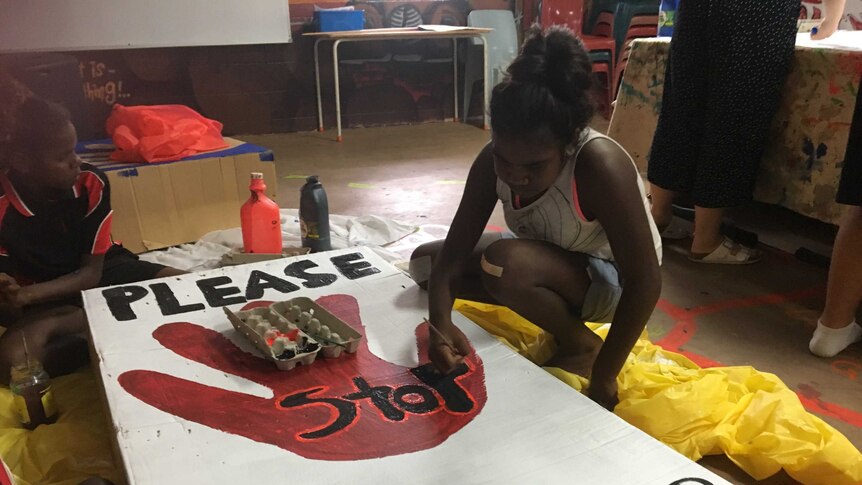 Two girls paint a sign against family violence.