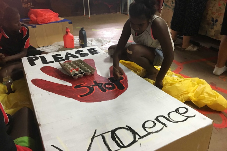 Two girls paint a sign against family violence.