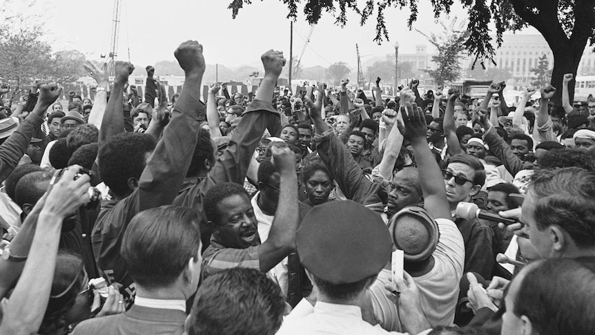 An old photo of black people with their fists in the air gathered under a tree in Washington DC.