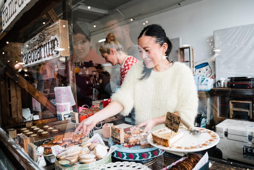 Two women work with baked goods behind a glass window.