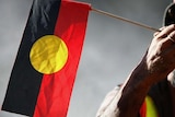 An elder holds an Aboriginal flag