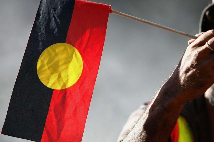 Indigenous elder holds an Aboriginal flag during Sorry Day.