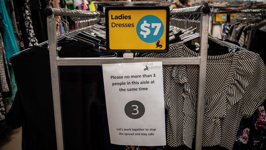 A clothing rack at Good Sammy with social distancing sign saying limit three people per aisle