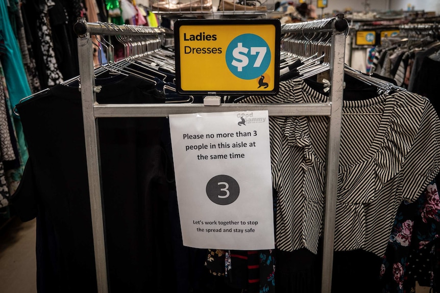 A clothing rack at Good Sammy with social distancing sign saying limit three people per aisle