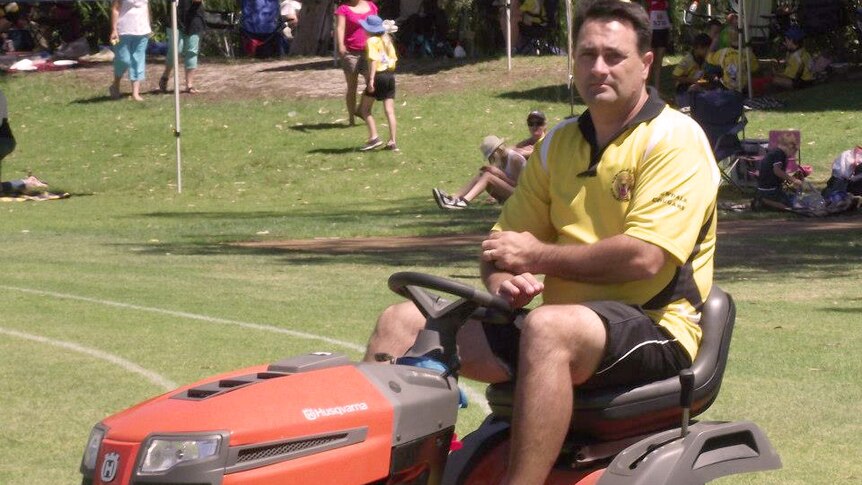 Bradley Robert Edwards sits on a red ride-on lawnmover on a grass oval in a yellow shirt.