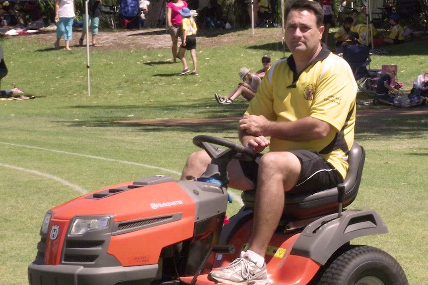 Bradley Robert Edwards sits on a red ride-on lawnmover on a grass oval in a yellow shirt.