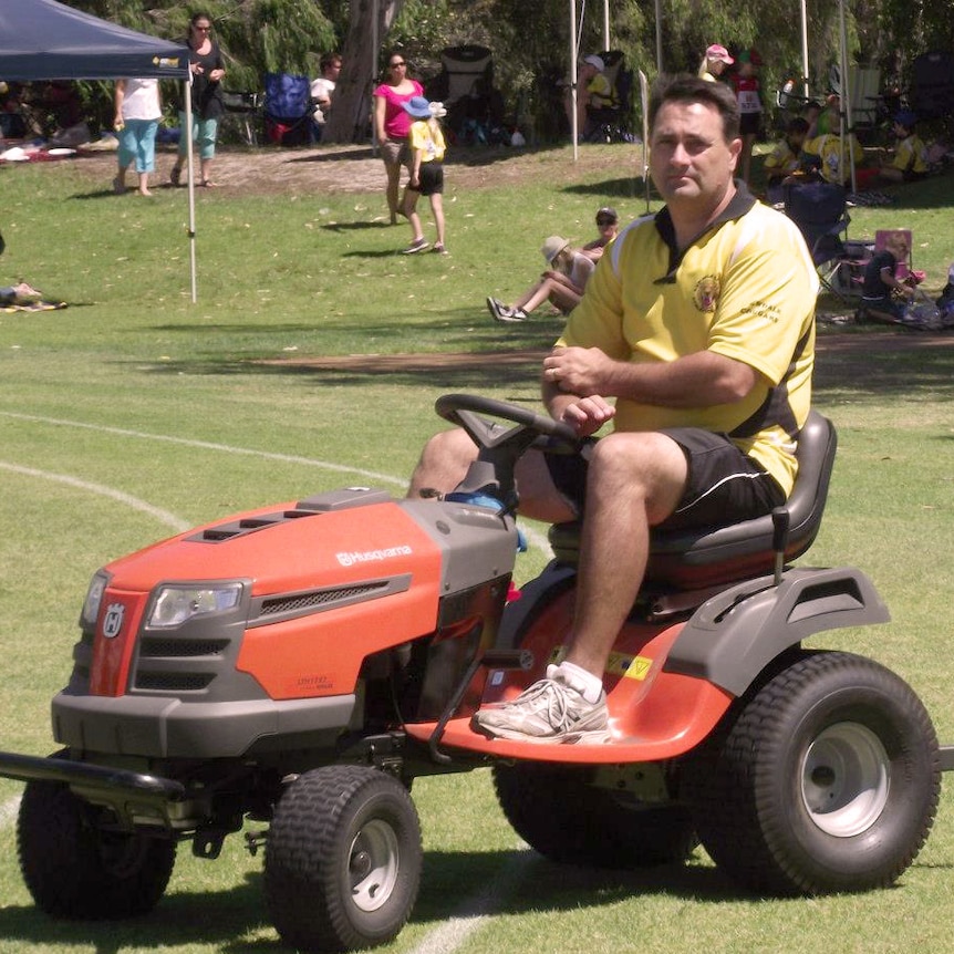 Bradley Robert Edwards sits on a red ride-on lawnmover on a grass oval in a yellow shirt.