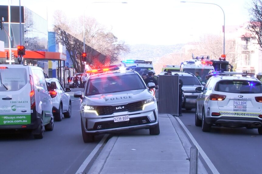 A police car parked on a median strip surrounded by other emergency vehicles. A grey barrier is set up