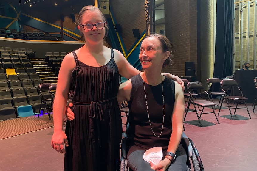 Two women are next to each other smiling in front of empty chairs