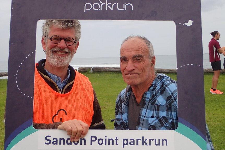 Erno van Alphen smiles holding a Sandon Point parkrun cardboard frame