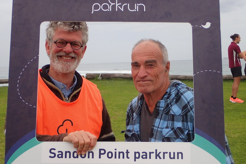 Erno van Alphen smiles holding a Sandon Point parkrun cardboard frame