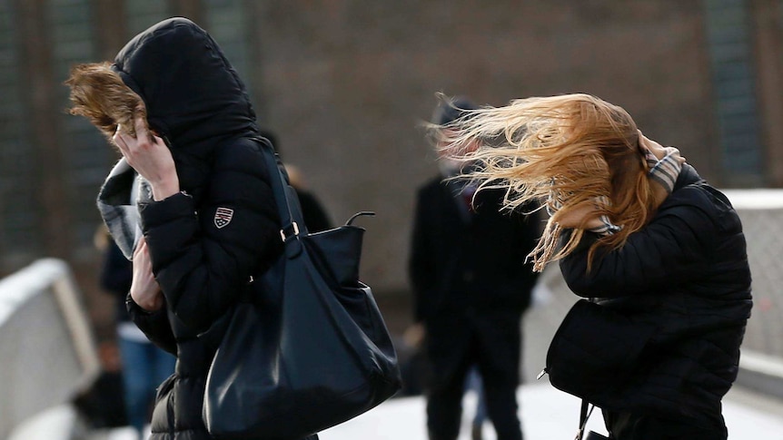 People crossing the Millennium Bridge in London cover their faces in windy weather.