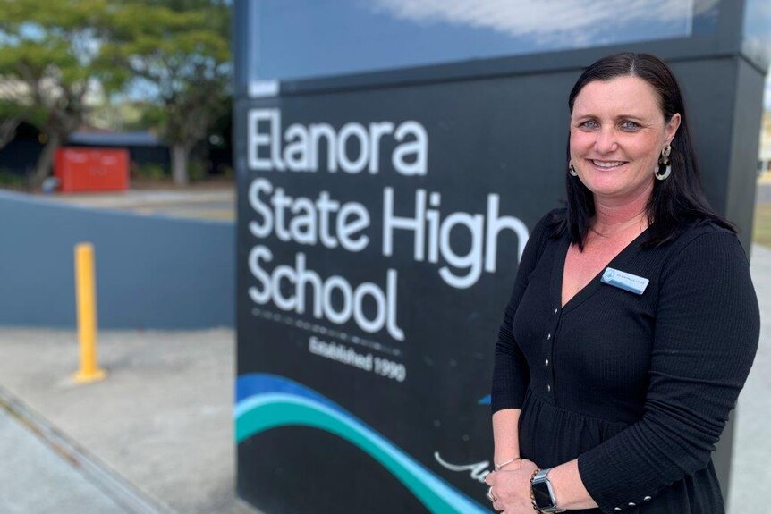 A woman in a black shirt stands in from of a sign which reads 'Elanora State High School'