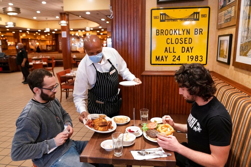 Waiter wearing a mask serves lunch to two men at Junior's Restaurant in New York.
