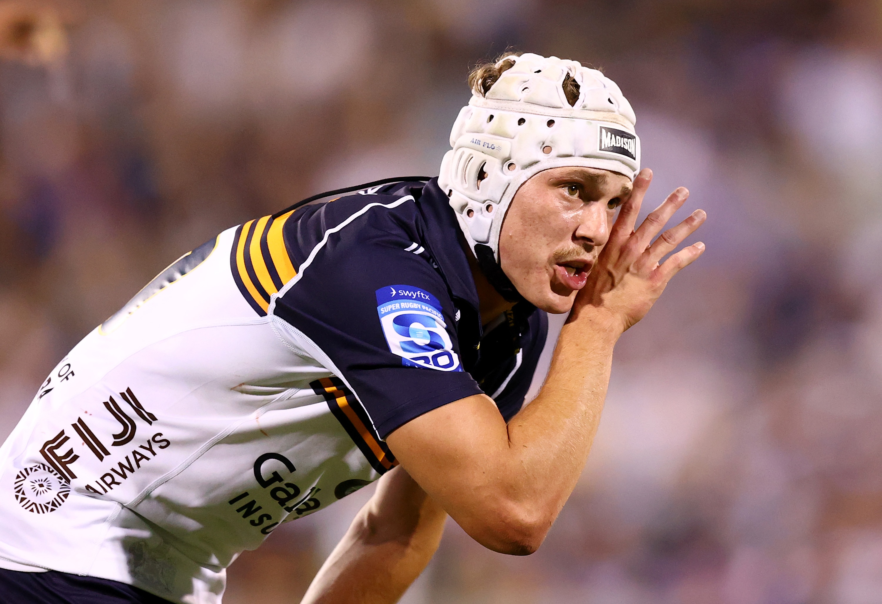 A footballer in a helmet whispers something to a teammate out of frame.