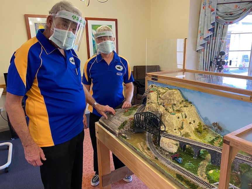 Two men in blue and yellow shirts beside train set