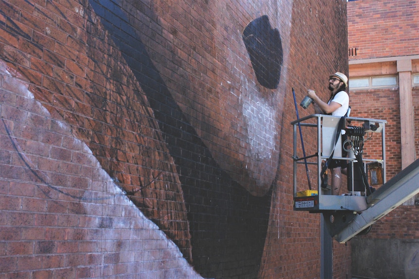 An artist on a cherry-picker painting a brick wall